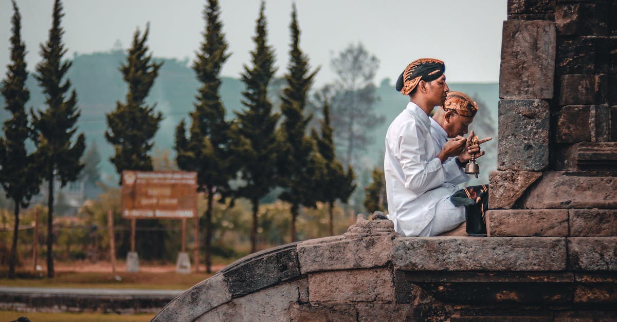 Side view of anonymous ethnic Buddhist male in traditional apparel praying near aged masonry church